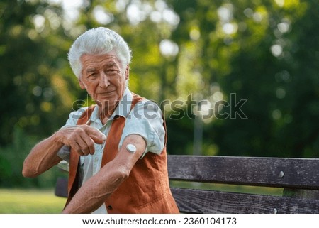 Senior man showing a sensor of continuous glucose monitor on his arm.