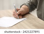 Senior man signing Last Will and Testament at wooden table indoors, closeup