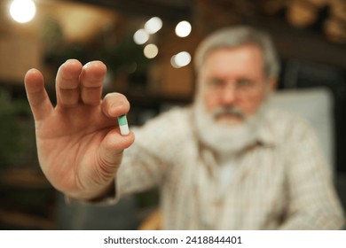 Senior man siting at home and drinking pills. Blurred background. Focus on hands with capsule, pill. Medication. Concept of health and medical care, aging, medicine, treatment - Powered by Shutterstock