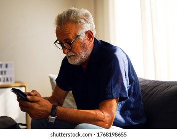 Senior man sitting alone in home and talking friend on smart phone.	
