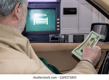 Senior man sitting in car with American dollars in his hand with bank ATM machine outside open window where he just made a transaction