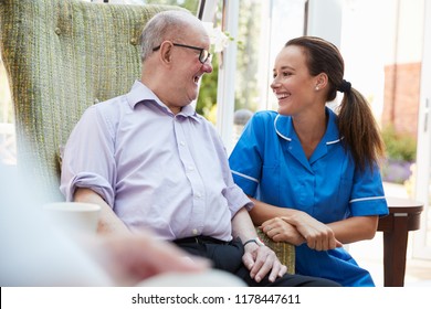Senior Man Sitting In Chair And Talking With Nurse In Retirement Home