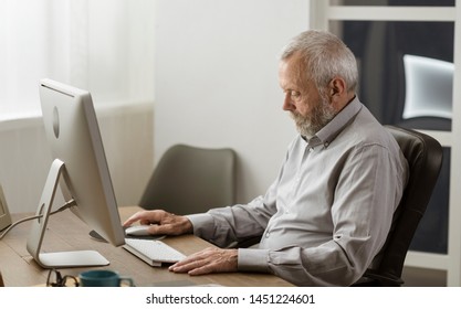 Senior Man Sitting At Desk And Using His Computer At Home