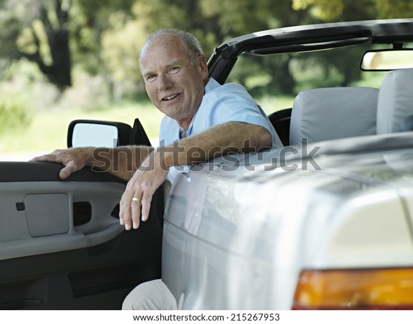 Senior man sitting in driver\'s seat of\
convertible car, smiling,\
portrait
