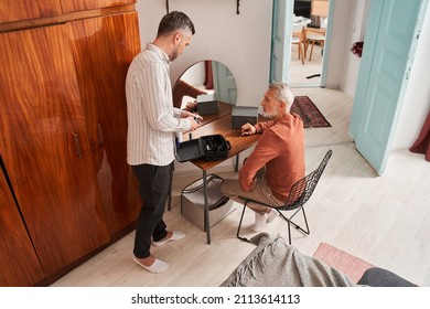 Senior Man Sitting In Front Of The Mirror And Preparing To Getting New Haircut From His Adult Son