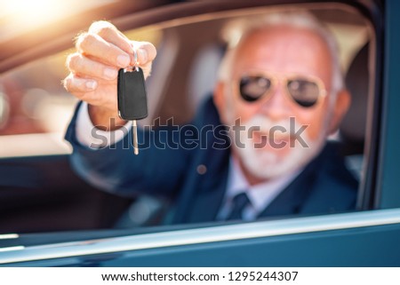 Senior man sitting in new car and showing car key.Selective focus on key.
