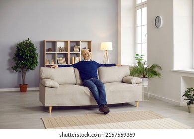 Senior man sitting on comfortable couch at home. Happy mature man relaxing on comfy grey sofa in cosy living room interior of his own house or apartment. People, lifestyle, comfort concept - Powered by Shutterstock