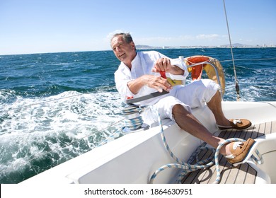 Senior man sitting on the deck of a yacht out at sea and leaning over the side of a boat while turning a rope pulley