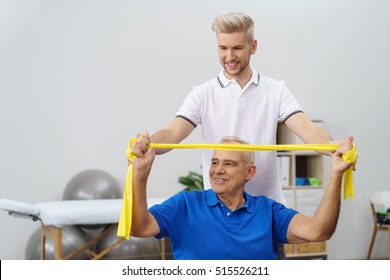 Senior Man Sitting On A Fitness Ball In Physical Rehabilitation Therapy With His Trainer