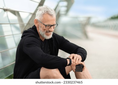 Senior man sitting on footbridge, checking smart watch, copy space. Stopwatch, positive elderly sportsman and runner check time, heart rate or monitor healthy body progress on data app - Powered by Shutterstock