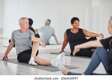 Senior man sitting on mat and doing relaxation exercises during yoga class with other people in studio