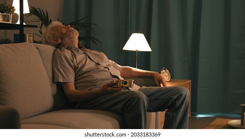 Senior Man Sitting On The Sofa And Sleeping While Watching TV At Night