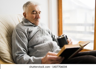 Senior man sitting and Reading a book at the retirement nursing home with cup of tea in hand - Shutterstock ID 1407706034