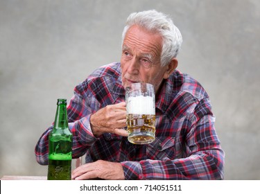 Senior Man Sitting At Table And Drinking Beer From Mug