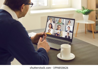 Senior man sitting at table having virtual group meeting with team of coworkers on laptop computer. Online business network communication, teamwork, home office workplace, hybrid work schedule concept