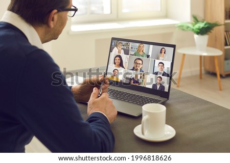 Senior man sitting at table having virtual group meeting with team of coworkers on laptop computer. Online business network communication, teamwork, home office workplace, hybrid work schedule concept
