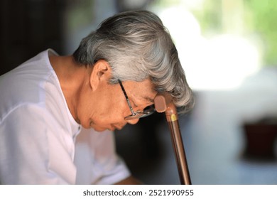 A senior man sitting thoughtfully while holding a walking cane, dressed in a white shirt and glasses. He appears to be in a peaceful, reflective moment, with natural sunlight highlighting his face.  - Powered by Shutterstock