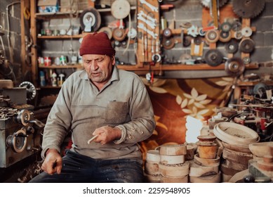 A senior man sitting in the workshop and processing wooden utensils in the old manual way