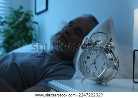 Senior man sleeping in bed at home, focus on alarm clock. Space for text