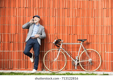 Senior man with smartphone and bicycle against brick wall. - Powered by Shutterstock