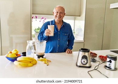 Senior man smiling confident holding glass of smoothie at kitchen - Powered by Shutterstock