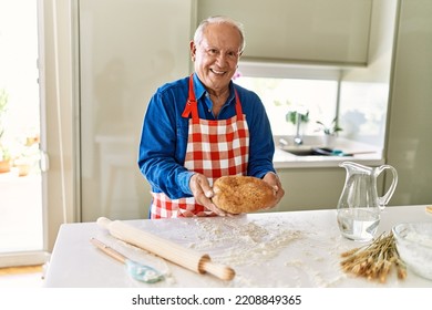 Senior man smiling confident holding homemade bread at kitchen - Powered by Shutterstock