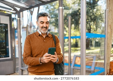 Senior man smiling using smartphone at bus stop