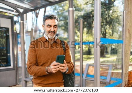 Senior man smiling using smartphone at bus stop