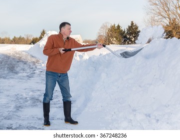 Senior Man With Snow Shovel Finishes Removing Snow Drifts On Driveway By Digging Out From The Blizzard