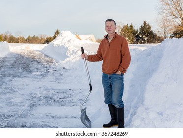 Senior Man With Snow Shovel Looking Content After Removing Snow Drifts On Driveway By Digging Out From The Blizzard