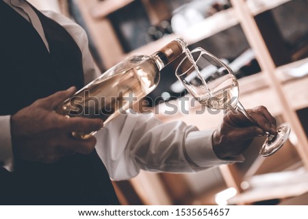 Senior man sommelier standing near cabinet pouring white wine into glass elegant close-up Foto stock © 