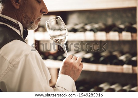 Senior man sommelier standing near cabinet holding glass smelling white wine closed eyes delightful close-up Foto stock © 