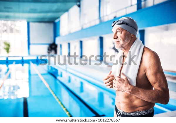 Senior man\
standing by the indoor swimming\
pool.