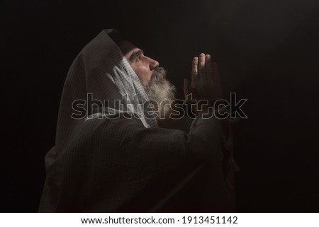 A senior man standing in dark smoky background light ray from above. Prayer gesture.