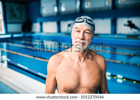Senior man standing in an indoor swimming pool.