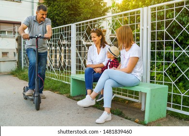 Senior man standing on the electric scooter by the bench with his family mother neighbor sitting on the bench by the fence in summer day - Powered by Shutterstock