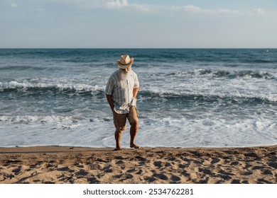 A senior man standing thoughtfully on the beach, gazing at the v - Powered by Shutterstock