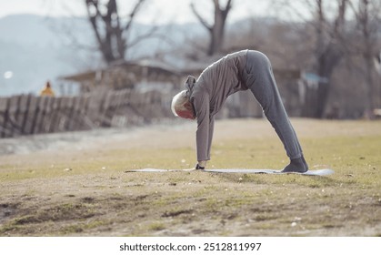 Senior man stretching body on yoga mat outdoor in early spring time. Healthy lifestyle in aging process - Powered by Shutterstock