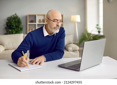 Senior man studying online at home. Focused adult student in glasses sitting at table with modern laptop computer, attending webinar, learning new things and taking notes. Online education concept - Powered by Shutterstock