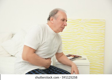 Senior Man Suffering From Abdominal Pain While Sitting On Bed At Home