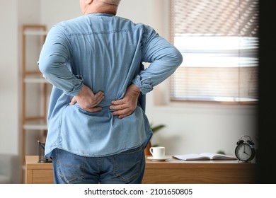 Senior man suffering from back pain near table at home - Shutterstock ID 2101650805