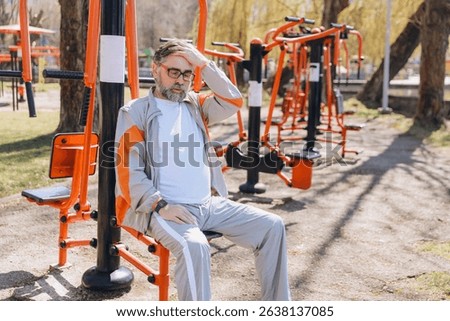 Senior man suffering from dizziness while exercising in an outdoor gym, touching his head with his hand