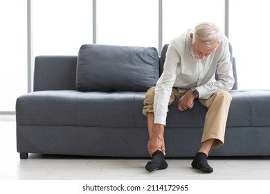 senior man suffering from knee ache on sofa - Shutterstock ID 2114172965