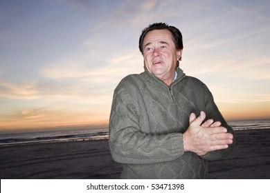 Senior Man In Sweater Rubbing Hands To Stay Warm On Beach