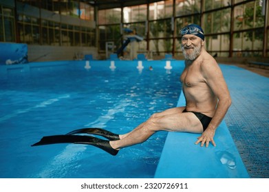 Senior man swimmer wearing on flippers while sitting at poolside