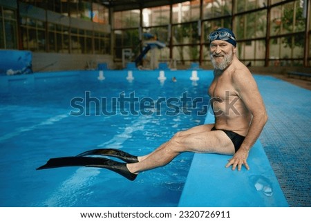Senior man swimmer wearing on flippers while sitting at poolside