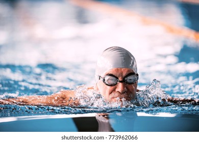 Senior Man Swimming In An Indoor Swimming Pool.