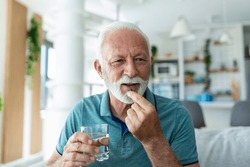 Senior Man Takes Pill With Glass Of Water In Hand. Stressed Mature Man Drinking Sedated Antidepressant Meds. Man Feels Depressed, Taking Drugs. Medicines At Work