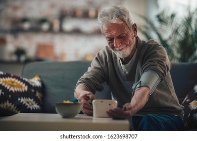 Senior Man Taking His Blood Pressure At Home In The Living Room On Sofa.