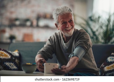 Senior Man Taking His Blood Pressure At Home In The Living Room On Sofa.